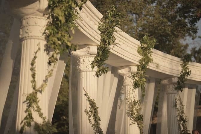 A curved white colonnade wrapped in trailing greenery and white blooms.