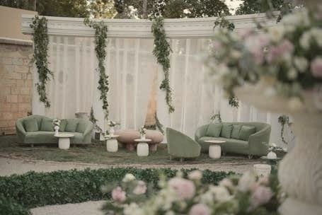 A garden lounge with sage sofas and blush flowers before a draped colonnade.