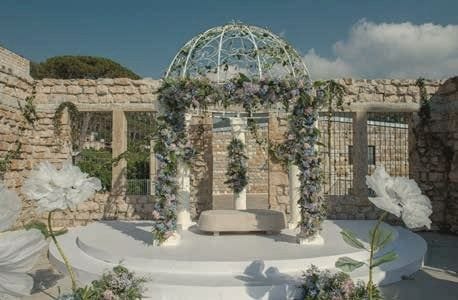 A domed garden pavilion dressed in white and lilac flowers within old stone walls.