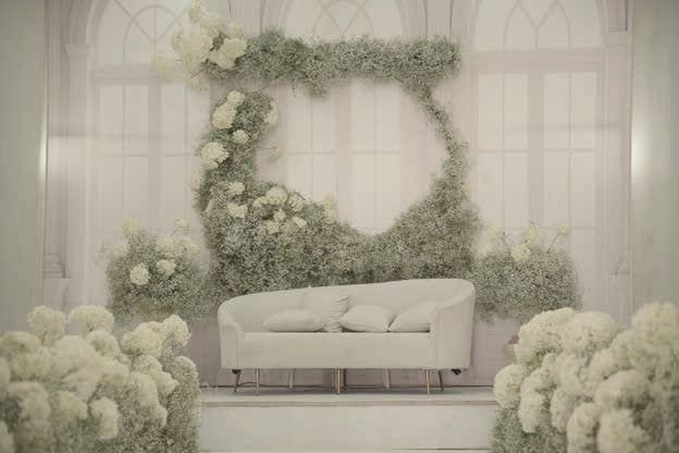 A white lounge setting framed by a crescent of white hydrangeas and greenery.